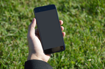 Male hand holding smart phone with grass background