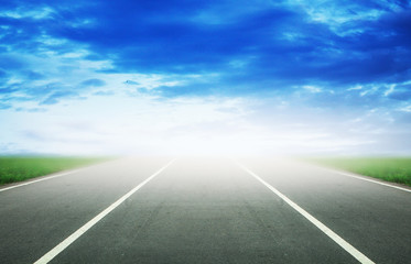 Background of blurred asphalt road, clear blue sky with clouds. Sunlit skyline