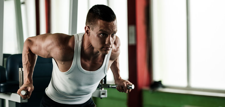 phisique fitness competitor works out in gym lifting dumbbells