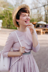 Inspired dark-haired girl wearing hat sincerely laughing during walk in park in weekend. Portrait...
