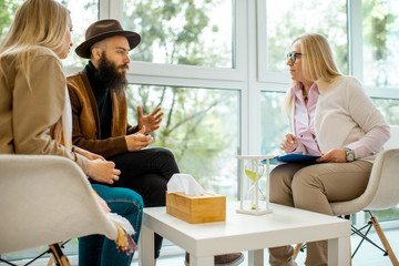 Young couple having misunderstandings during the psychological counseling with senior female psychologist in the office