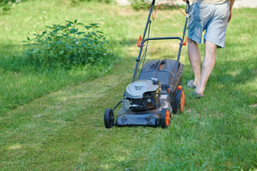 European man is mowing the lawn on his countryside plot. © Artem