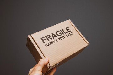 Fragile handle with care warning text on small cardboard with text sign in man's hand against gray background - transportation of delicate objects and good - vintage color cast.