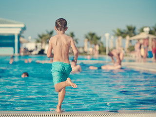 Caucasian boy run to make jump into swimming pool water.