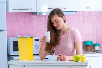 Happy attractive woman holding glass of fresh milk and spoon of crispy chocolate balls for cereals...