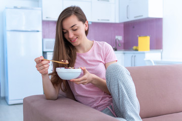 Young, happy beautiful brunette woman in pajamas eating chocolate balls for cereals breakfast at home