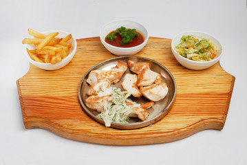 A set of french fries, salad, sauce and fried pieces of meat on a board on a gray isolated background