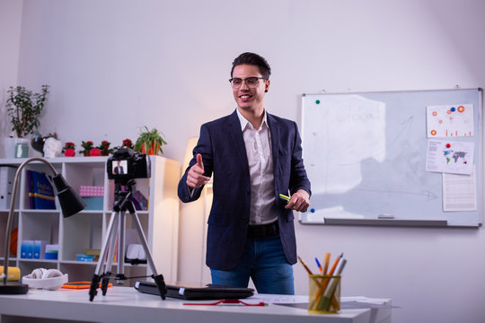 Smiling positive young blogger showing thumbnails on camera