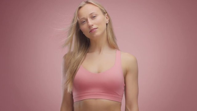 blond model in studio on pink background with hair blowing in air watching to the camera and touches he rneck