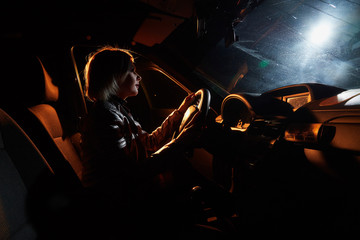 Fototapeta na wymiar Fashionable young woman in a car in the night and colour light behing her