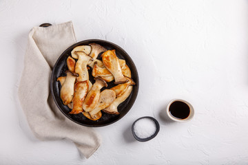 Fried eryngii mushrooms in cast-iron pan on white table. Grilled slices of king oyster mushrooms. Top view, copy space.