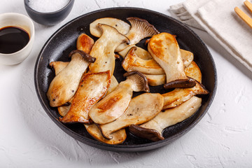 Fried eryngii mushrooms in cast-iron pan on white table. Grilled slices of king oyster mushrooms.