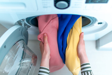 Loading colored clothes and linen in washing machine. Doing laundry at home. Top view