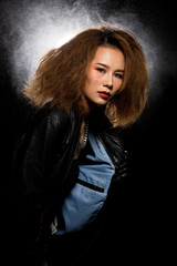 Fototapeta premium Fashion Asian Woman Tan skin Afro fu hair eyes beautiful make up black bra jacket silver necklace posing, Studio Lighting Dark Background back rim light with steam smoke effect