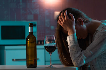 Unhappy, lonely stressed woman with red wine is drinking alone in the kitchen in evening. Life difficulties and problems. Female alcoholism and alcohol addiction