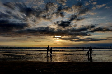 Fototapeta na wymiar tourists while enjoying the sunset on Kuta beach, with an exciting atmosphere, the color of the sky is golden and the weather is sunny, so visitors are very comfortable to linger
