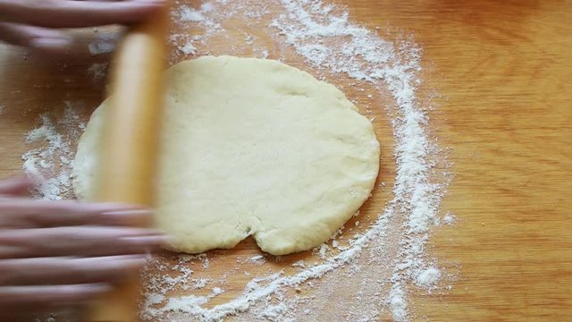 Female hands rolling dough with rolling pin for pastry on wooden table