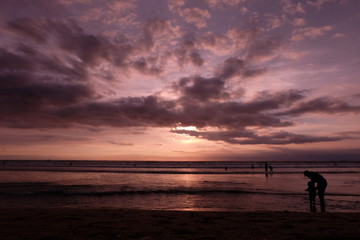 Fototapeta premium tourists while enjoying the sunset on Kuta beach, with an exciting atmosphere, the color of the sky is golden and the weather is sunny, so visitors are very comfortable to linger
