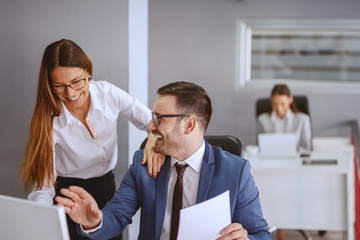 Smiling Caucasian businessman sitting at his workstation and talking to his female colleague. Trust...