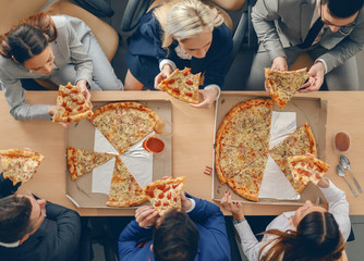 Top view of business people in formal wear sitting at table and having pizza for lunch.