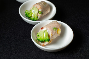 Meat rolls, with cheese and broccoli on white plates.