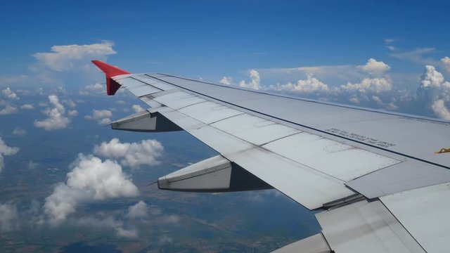 4K footage. traveling by air. aerial view through an airplane window with light from len flare . wing airplane and beautiful white clouds in blue sky for background