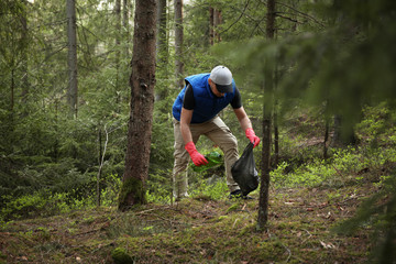 Man cleans garbage and plastic bottle in forest. Green volunteering. Caring for environment.