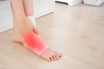 Obraz na płótnie Canvas Closeup of a Foot with Gauze Elastic Bandage. Asian Woman Ankle Injury Runner. Hands on Injured Legs and Feet with Red Spot on Pain Area Sitting on a Wooden Floor Background from Rupture or Tear.
