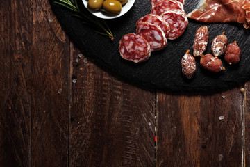 Cutting board with prosciutto, salami, cheese,bread and olives on dark stone background