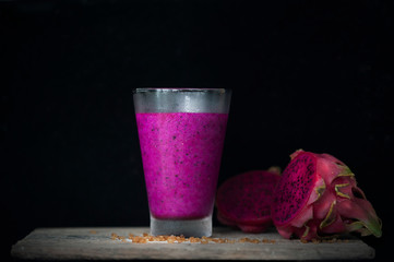 Red Dragon fruit juice on wooden surface, solid black background, still life shooting style.