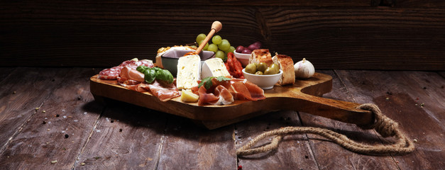 Cutting board with prosciutto, salami, cheese,bread and olives on dark wooden background