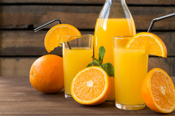 orange juice in glasses with a sprig of mint, half of fresh orange, on a wooden background