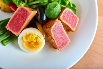 Nicoise salad with grilled tuna and boiled egg on a wooden background, close-up