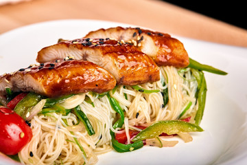 Asian noodles of funchoz with chopped vegetables and marinated chicken. Wooden background, close-up.