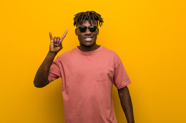 Young casual black man wearing sunglasses showing a horns gesture as a revolution concept.