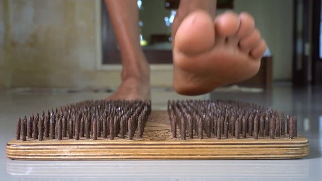 Male feet step on a wooden yoga board with lot of metal nails pins. Close up of yoga board with sharp nails