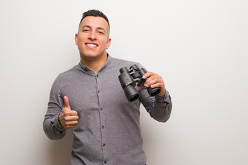 Fototapeta na wymiar Latin man smiling and raising thumb up. He is holding a binoculars.
