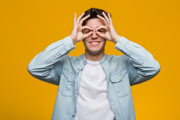 Young handsome student wearing a denim shirt showing okay sign over eyes