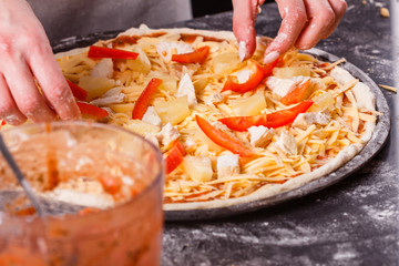 young woman in a gray aprons prepares a Hawaiian pizza
