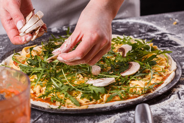 young woman in a gray aprong prepares a vegetarian pizza