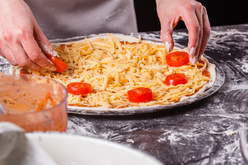 young woman in a gray aprong prepares a vegetarian pizza
