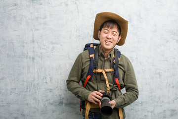 Fototapeta premium Young chinese explorer man holding a camera cheerful with a big smile