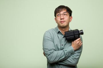 Young chinese man holding a vintage camera smiling confident and crossing arms, looking up