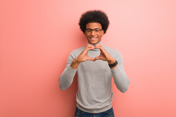 Young african american man over a pink wall doing a heart shape with hands