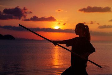 Young beautiful girl woman blond doing kung fu with bamboo stick on the seashore at sunset