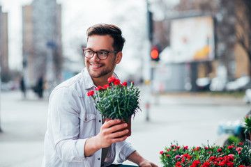 Positive young man buying flowers outdoors.