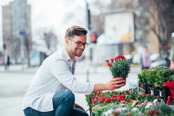 Young man choosing flowers in flower shop outdoors.