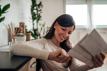 Smiling woman looking at received mail at home, close-up.