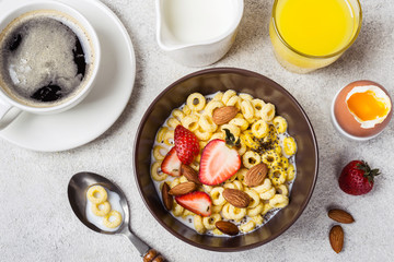 Bowl with cereal rings cheerios, strawberries and milk. Fresh coffee, orange juice and egg. Balanced breakfast concept
