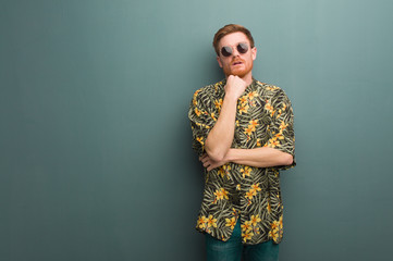 Young redhead man wearing exotic summer clothes tired and bored